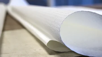 Nahaufnahme einer weißen Tapetenrolle, die auf einem Holztisch liegt. Glasfaster Raufaser